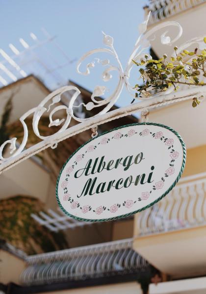 Insegna dell'Albergo Marconi, decorata con rose, sotto un cielo azzurro.