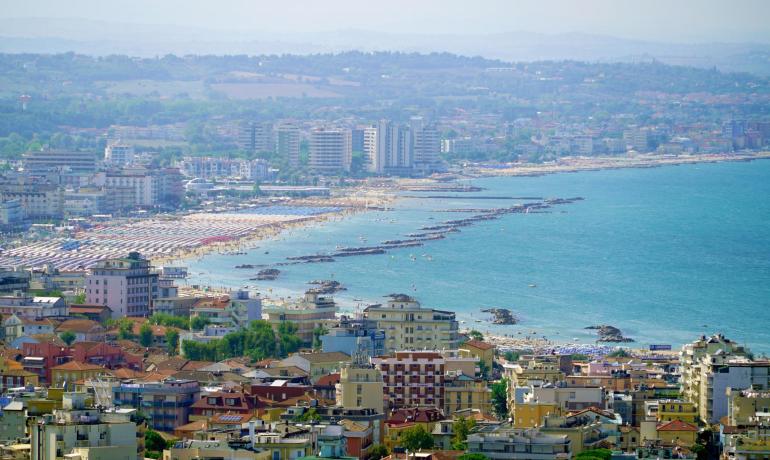 Vista panoramica di una città costiera con spiaggia affollata.